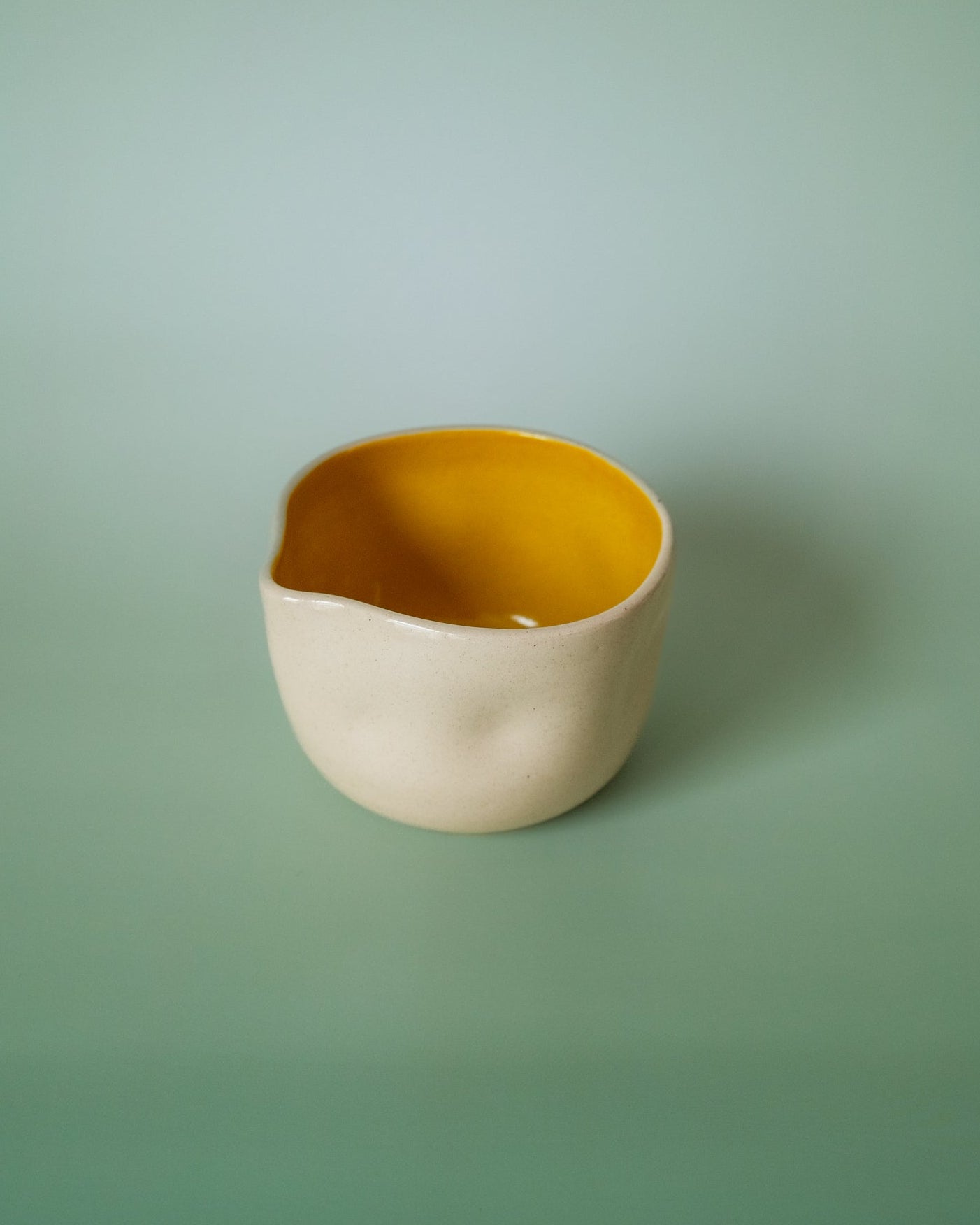 Ceramic bowl with yellow interior and beige exterior on a green background